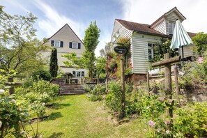 Un jardin avec un banc en bois, un mur de pierre et une maison avec un toit à deux versants.