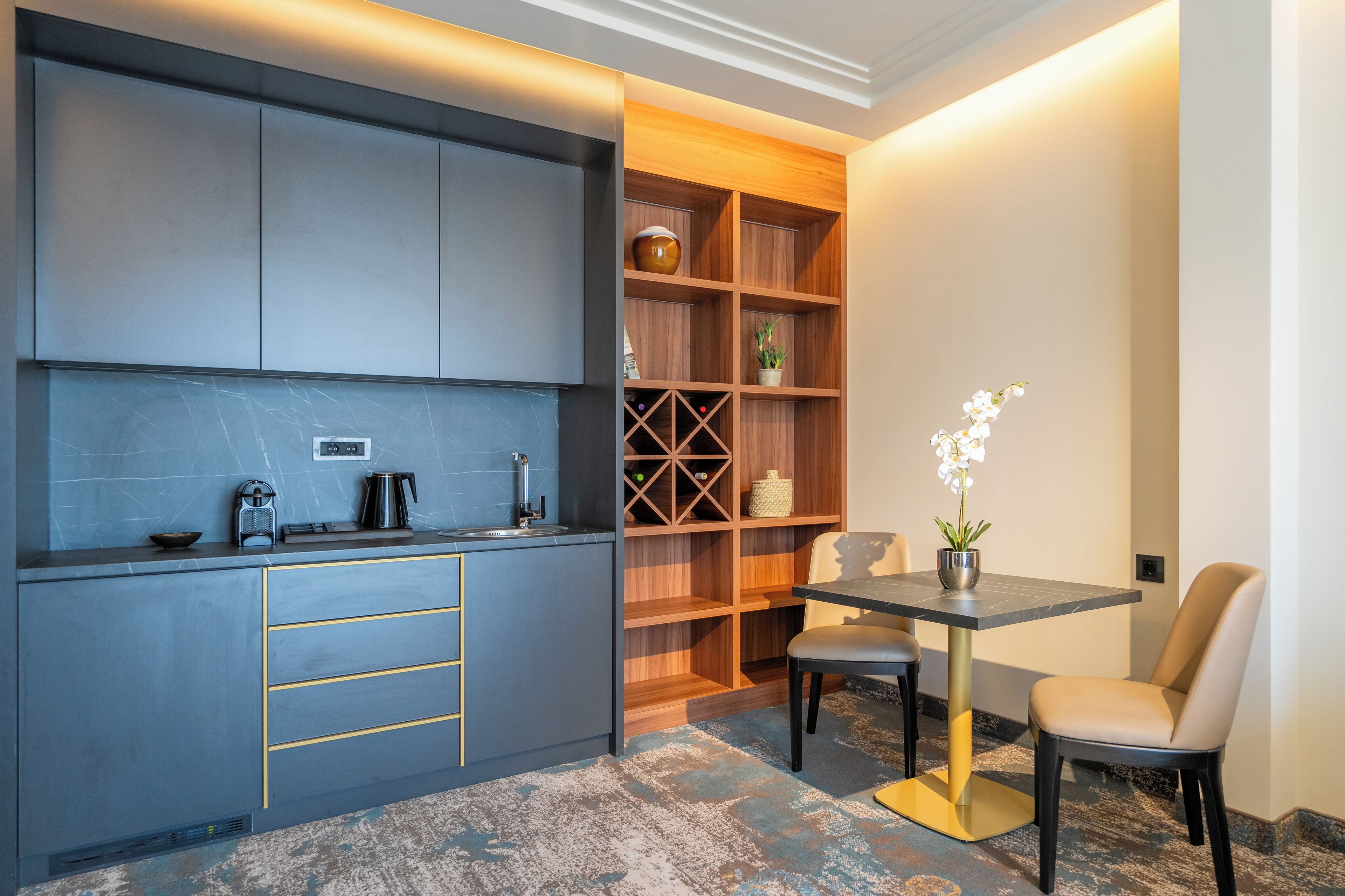 A modern kitchen with grey cabinets, a wooden shelving unit, and a dining area with a table and chairs.