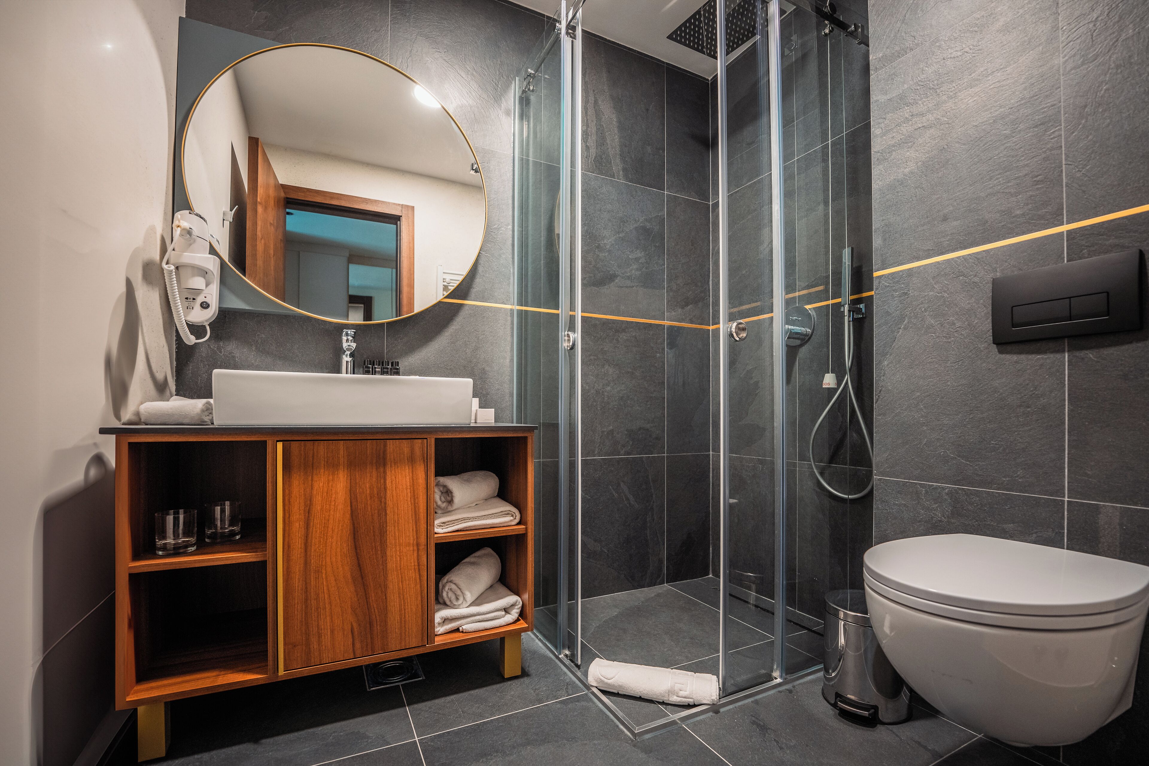 Un baño moderno con ducha de vidrio, tocador de madera con espejo y un inodoro blanco.