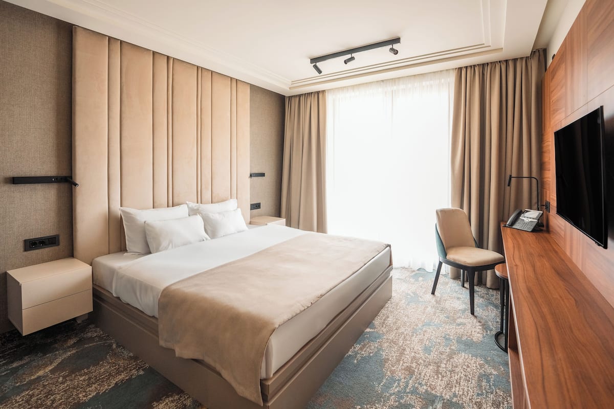 A hotel room with a large bed, a desk with a telephone, a TV, and a chair.