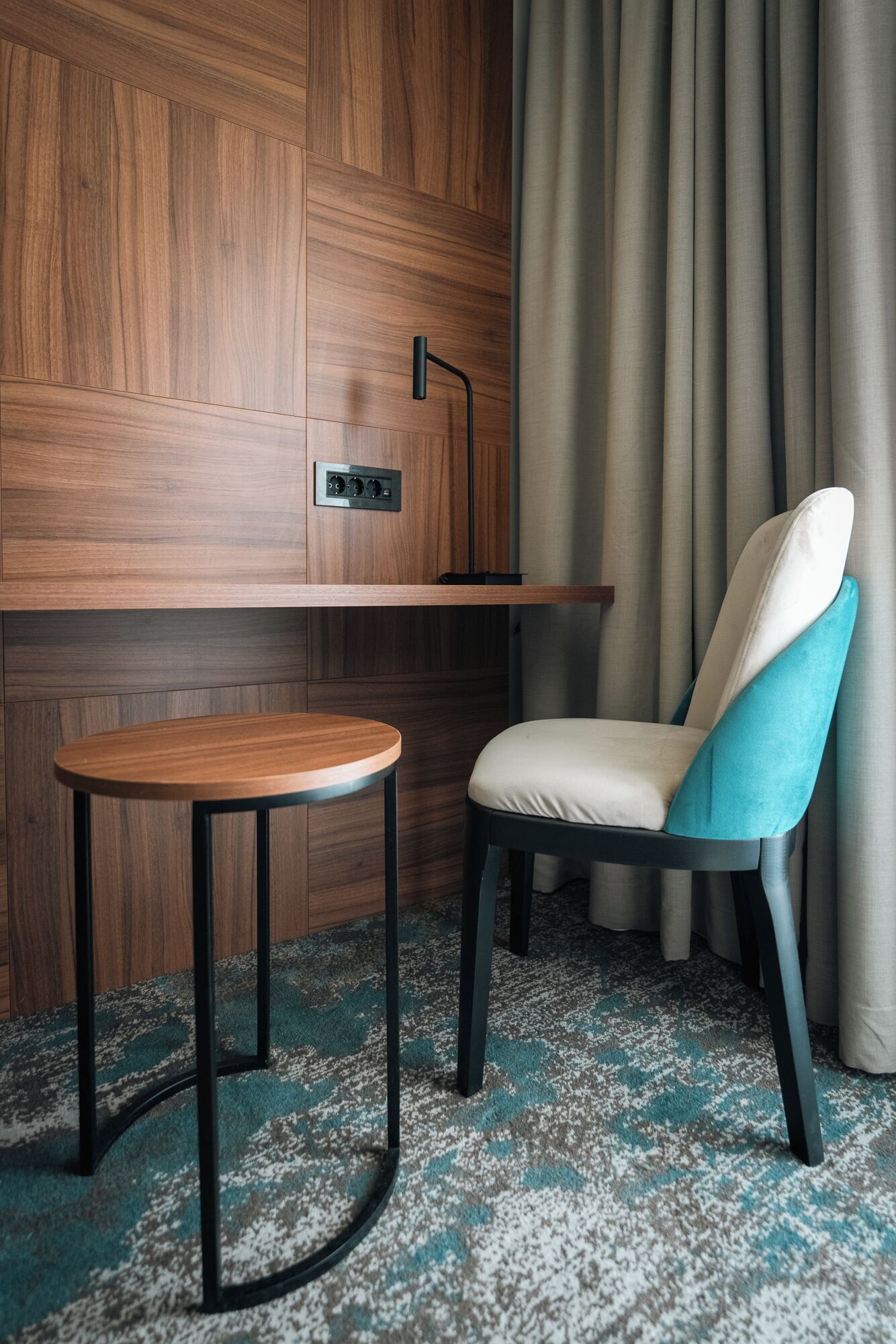 Ein modernes Zimmer mit einer Wandpaneele aus Holz, einem kleinen runden Tisch, einem Stuhl mit blauer Sitzkissen und einer Stehlampe.