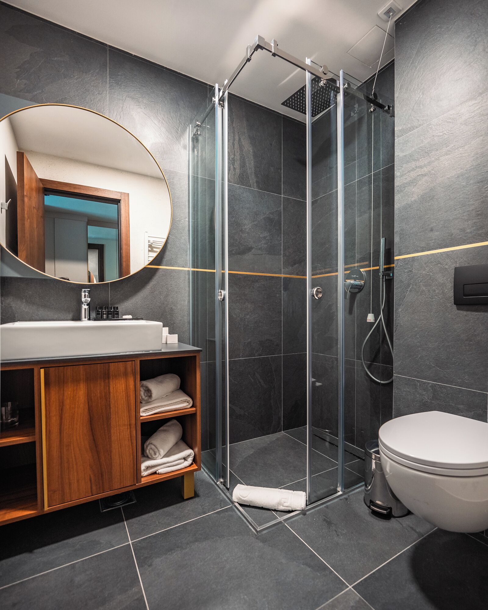 Un baño moderno con ducha de vidrio, tocador de madera con lavamanos y un inodoro.