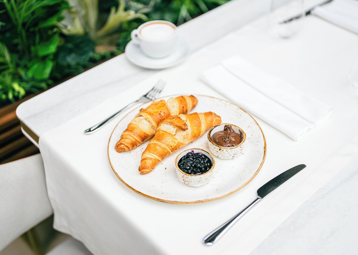 A breakfast setup with croissants, jam, and a cup of coffee on a white table.