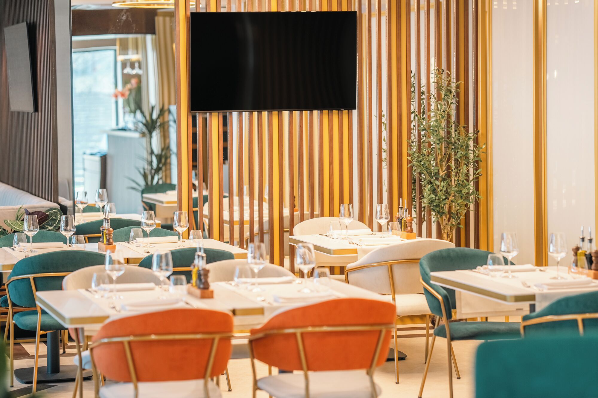 A restaurant with tables set for dining, a TV mounted on the wall, and vertical wooden panels.