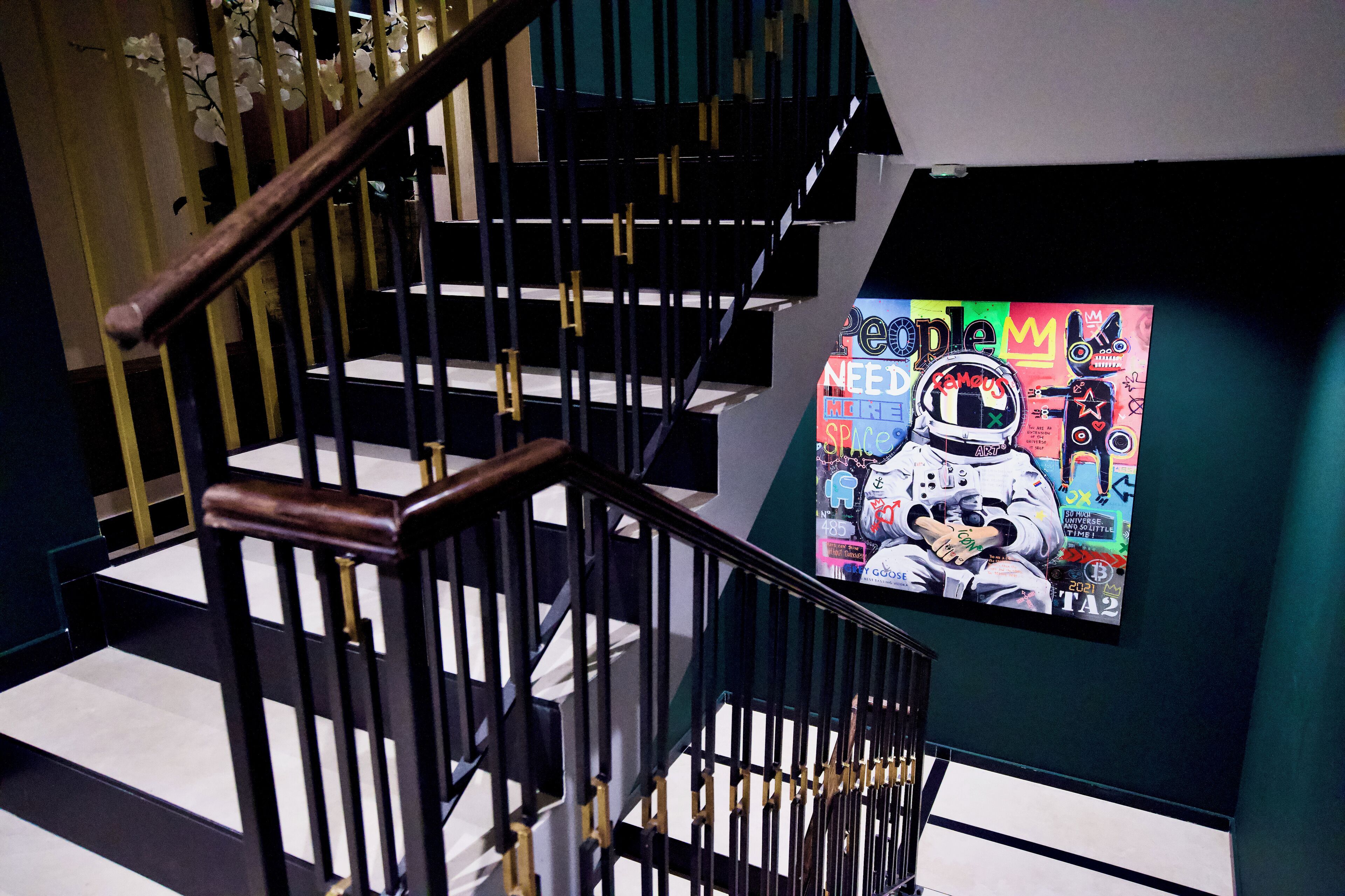 A staircase with black railings and wooden handrails, leading to a landing with a colorful poster featuring an astronaut.