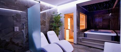 A modern spa room with a glass shower enclosure, two white lounge chairs, a massage table, and a starry sky ceiling.