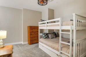 Een stapelbed met een houten dressoir en een lamp in een kamer met beige wanden en vloerbedekking.