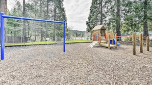 Ein Spielplatz mit einer blauen Schaukel, einem hölzernen Spielhäuschen und einer Rutsche.