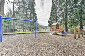 A playground with a blue swing set, a wooden playhouse, and a slide.