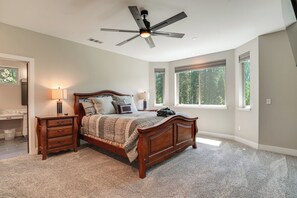 A bedroom with a wooden bed, a ceiling fan, a nightstand, a lamp, and large windows.