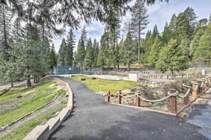 A paved pathway curving through a park with a grassy area, wooden fence posts, and a building in the background.