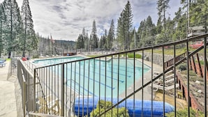 Ein Schwimmbecken, umgeben von hohen Bäumen, mit einer Holzterrasse und einem Metallgeländer.