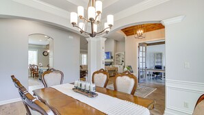 Un coin repas avec une table en bois, des chaises, un lustre et une vue sur la cuisine.