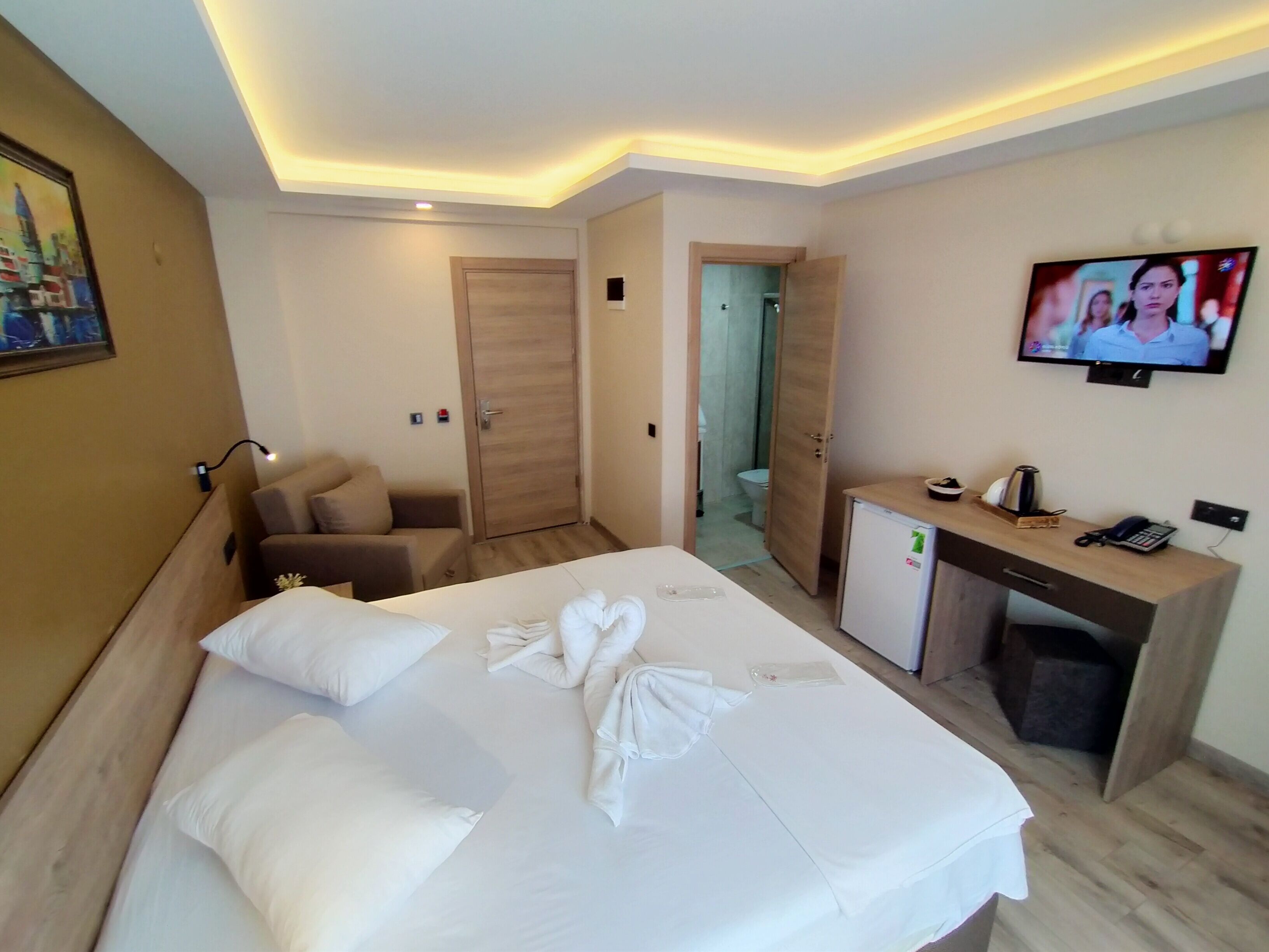 A hotel room with a bed, a desk, a TV, and a door leading to a bathroom.