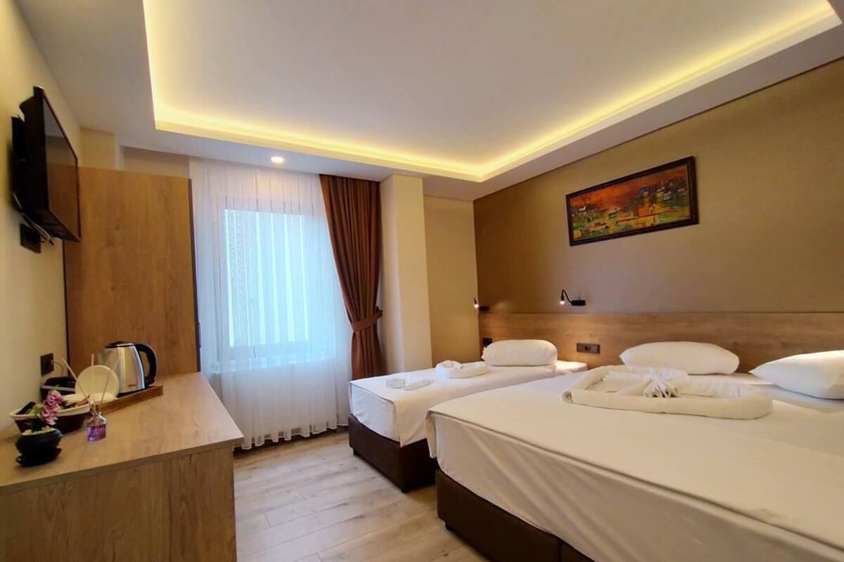 Een hotelkamer met twee bedden, een houten bureau, een schilderij aan de muur en een raam met gordijnen.
