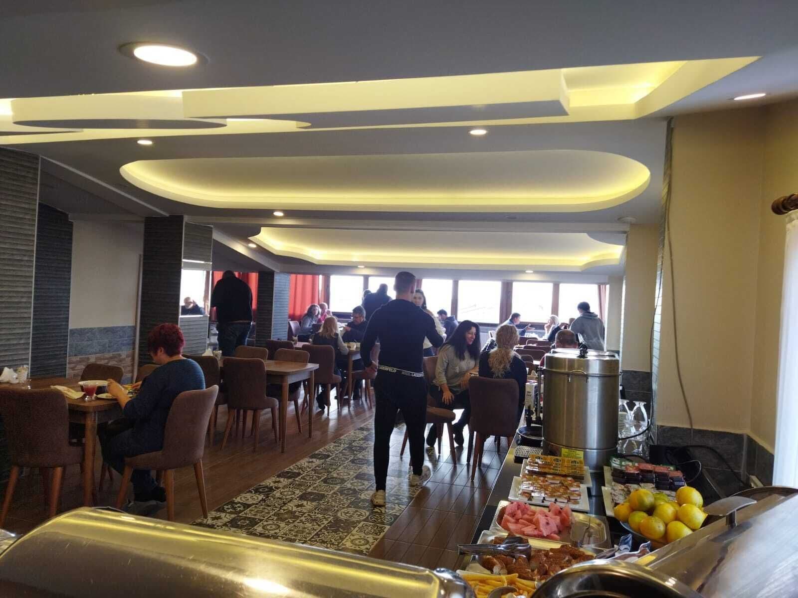A buffet area with a variety of food items, including fruits and meats, in a spacious dining hall with modern ceiling design and natural lighting.