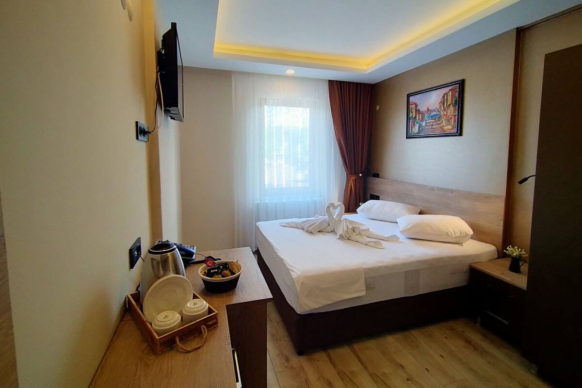 Een hotelkamer met een bed, een nachtkastje met een lamp, een schilderij aan de muur en een raam met gordijnen.