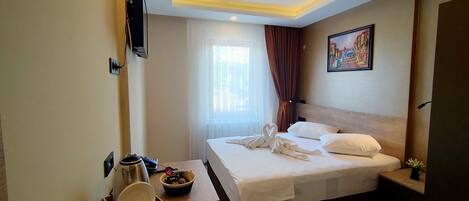 A hotel room with a bed, a bedside table with a lamp, a painting on the wall, and a window with curtains.