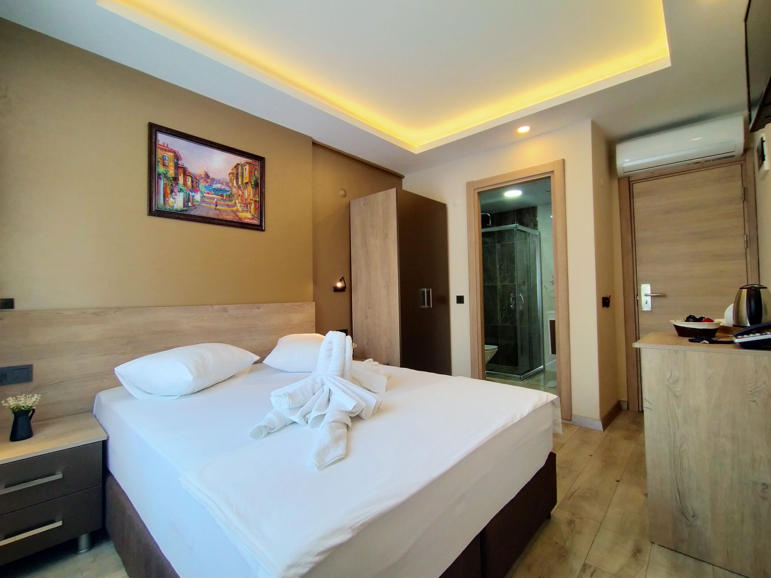 A hotel room with a neatly made bed, a painting on the wall, a wardrobe, and a shower area.