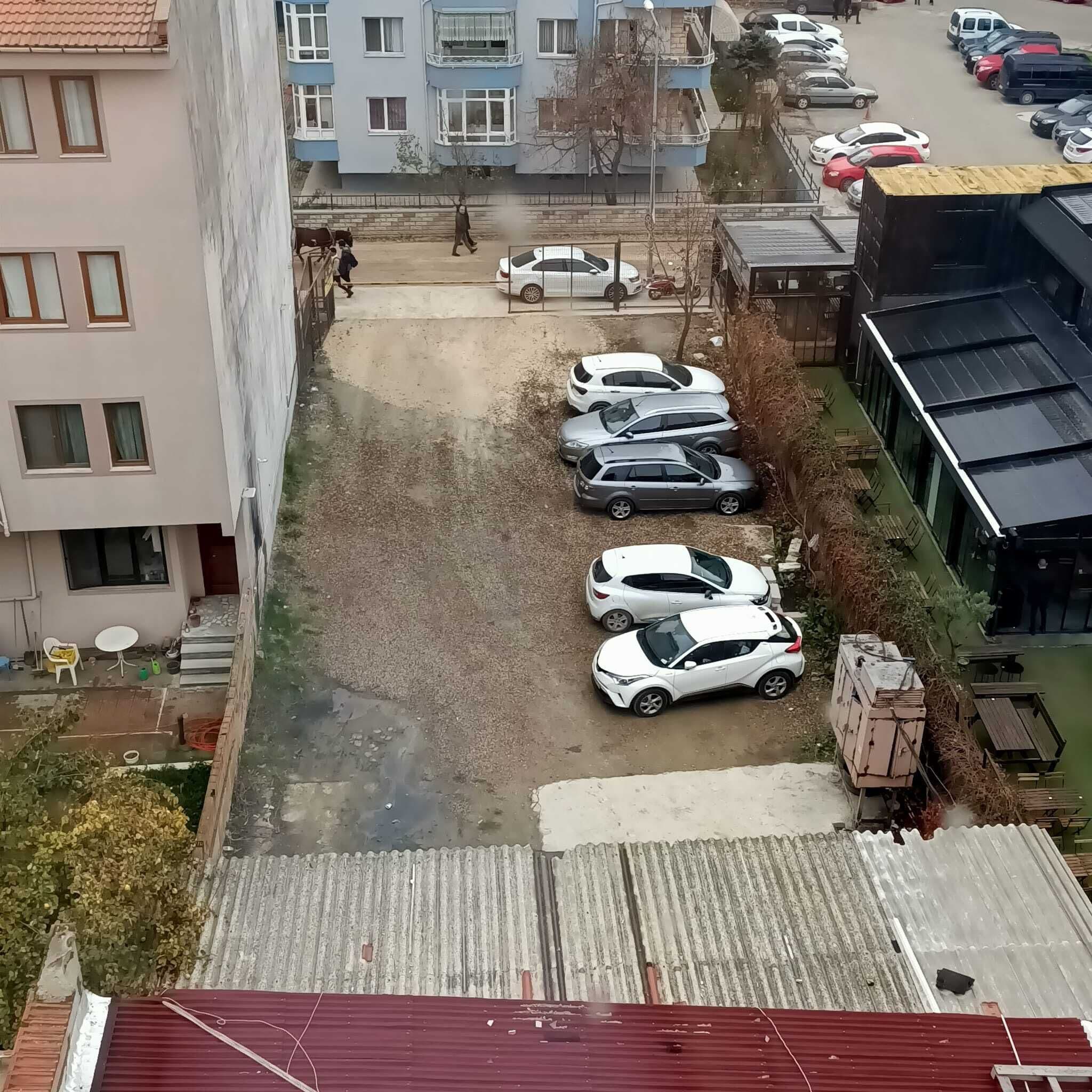 Un estacionamiento con varios coches, un edificio de techo rojo y un edificio residencial de varios pisos al fondo.