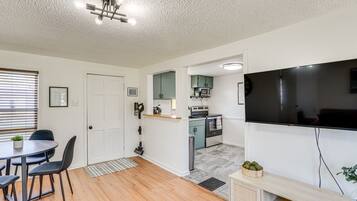 A modern kitchen with a flat-screen TV, wooden cabinets, and a dining area with a table and chairs.