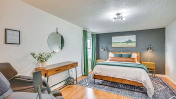 A bedroom with a bed, bedside tables, a desk, a chair, a mirror, and a potted plant.