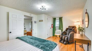 Un dormitorio con cama, sillón de masajes, escritorio y cortina verde.