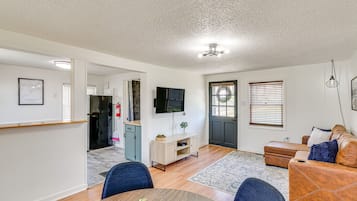 A modern living room with a dining area, a flat-screen TV mounted on the wall, and a door leading to another room.