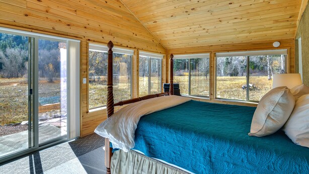 A wooden cabin bedroom with a large bed, a wooden ceiling, and large windows offering a view of the outdoors. - Close to Hot Springs: Chalk Creek Meadows Home! (Nathrop)
