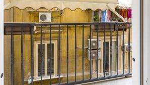 En balkon med gelænder i metal, et beige markise og klimaanlæg.
