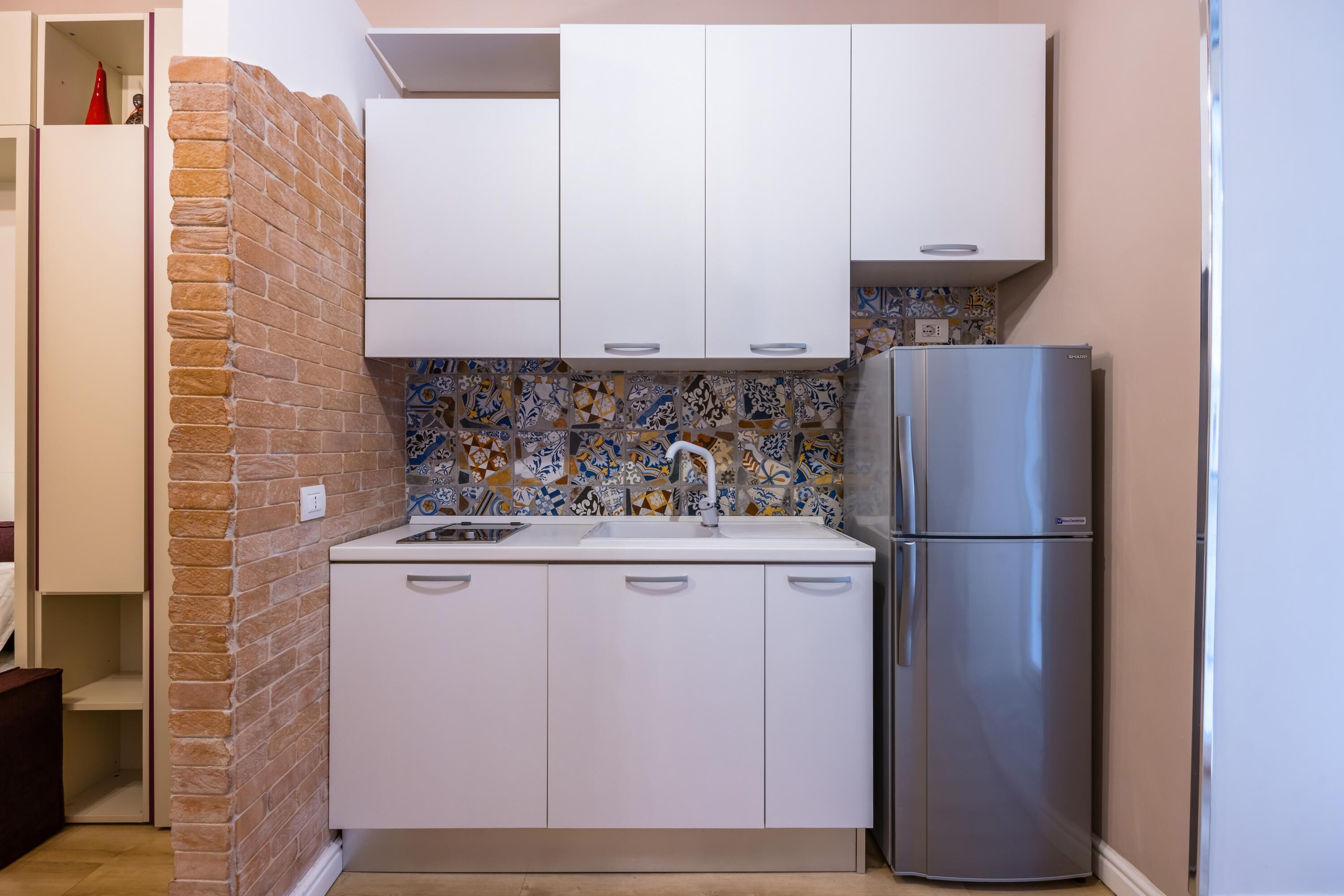A compact kitchen with white cabinets, a stainless steel refrigerator, and a tiled backsplash.