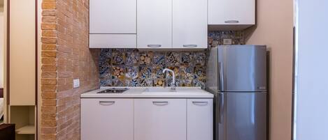 A compact kitchen with white cabinets, a stainless steel refrigerator, and a tiled backsplash.
