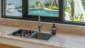 A kitchen with a large window overlooking a pool and garden.