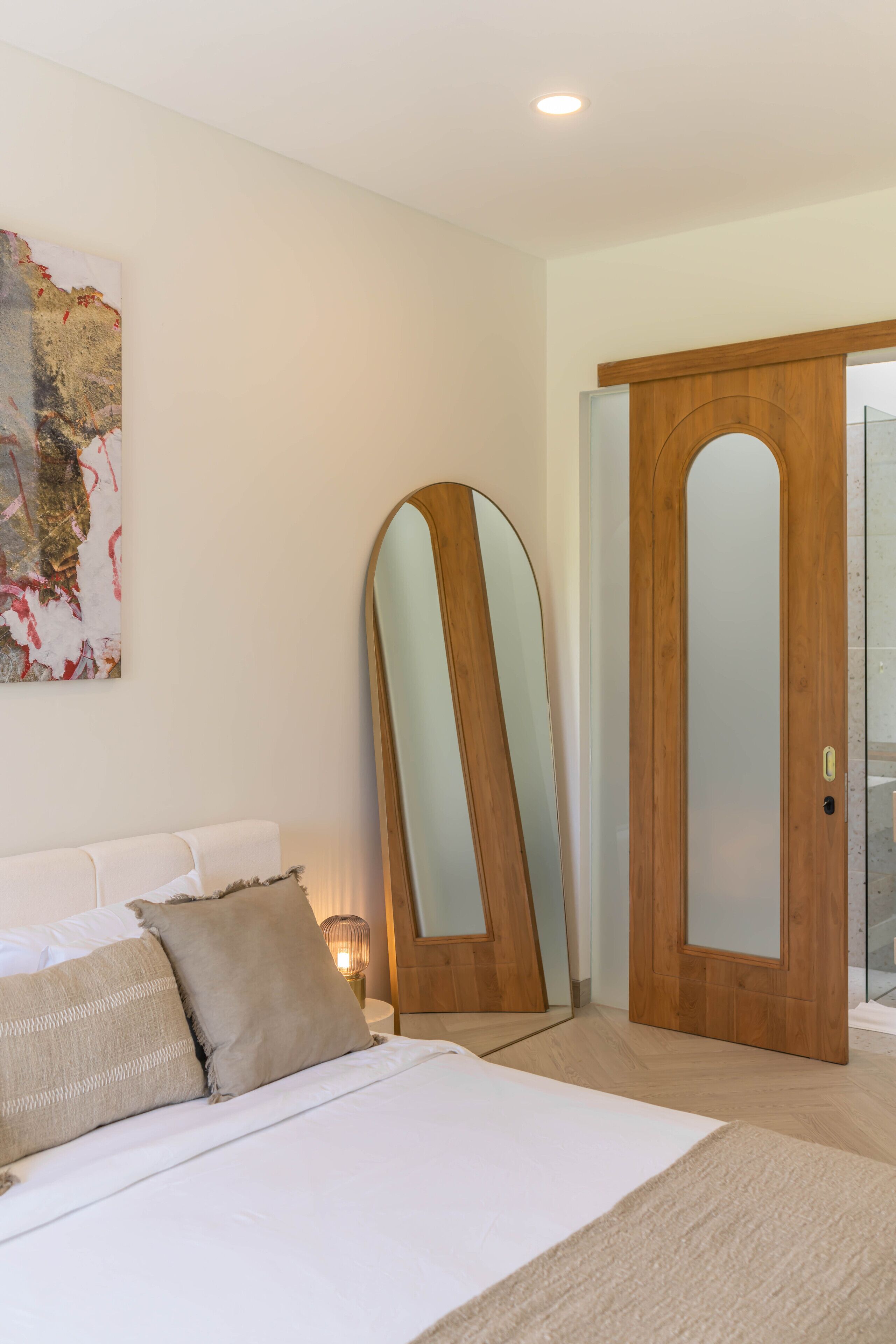 A bedroom with a bed, a large mirror, and a wooden door.