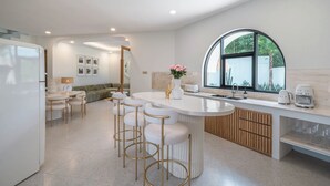 A modern kitchen with a central island, bar stools, and a large window.