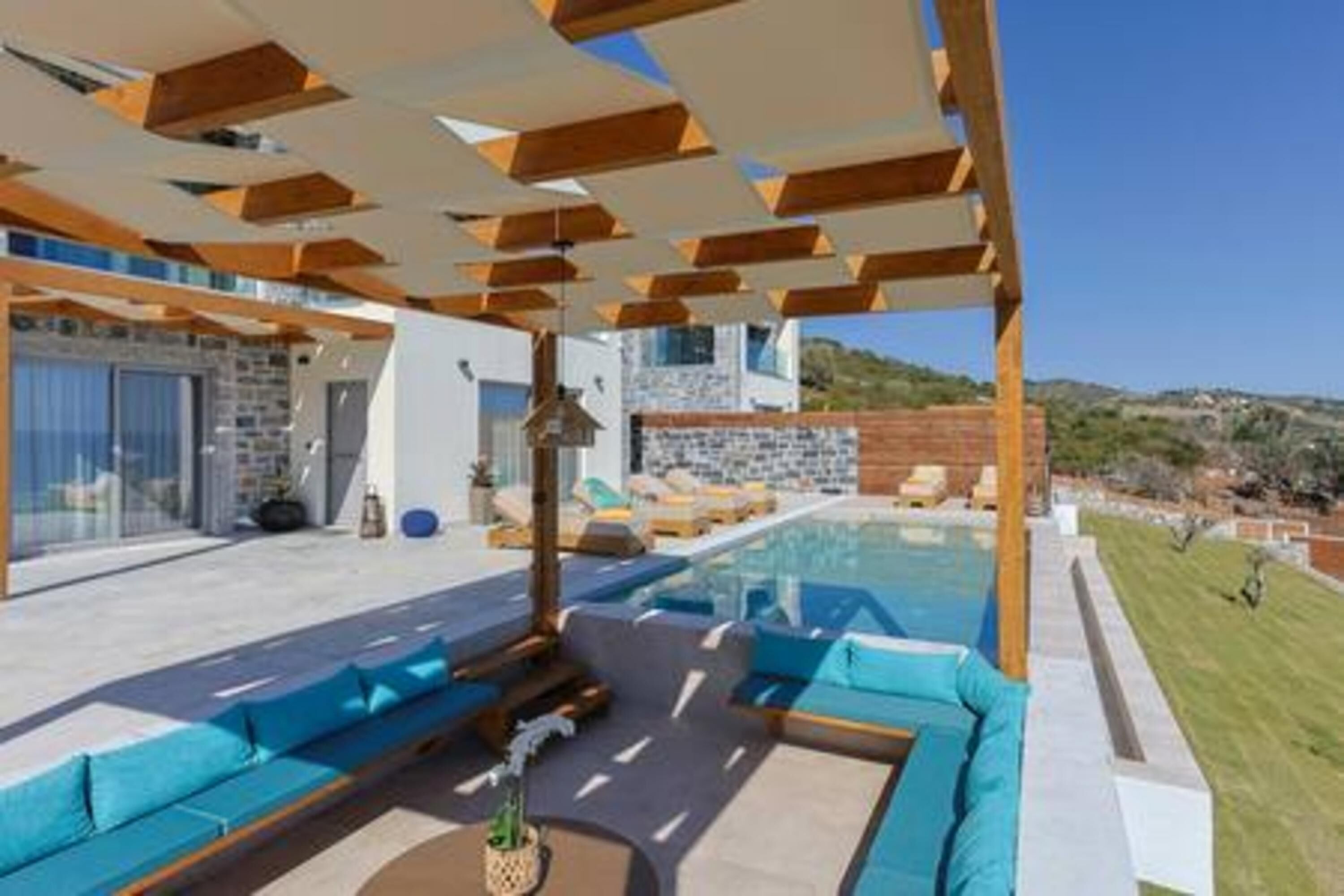 Een modern buitenzwembadgedeelte met een houten pergola, een zithoek met kussens en uitzicht op het omliggende landschap.