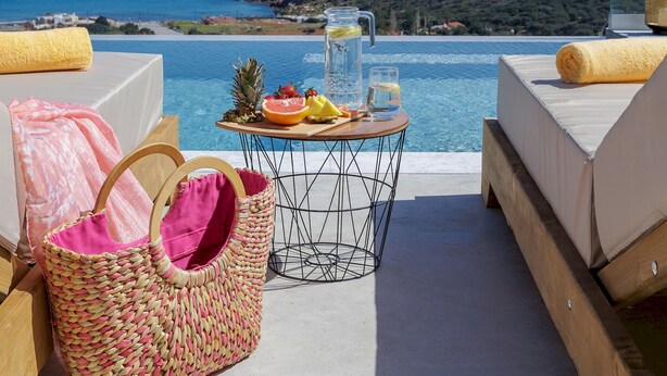 A poolside area with a view of the sea, a table with fruits and a drink, and wicker furniture. - Sunny Drops Blue Villa by Estia (Mylopotamos)