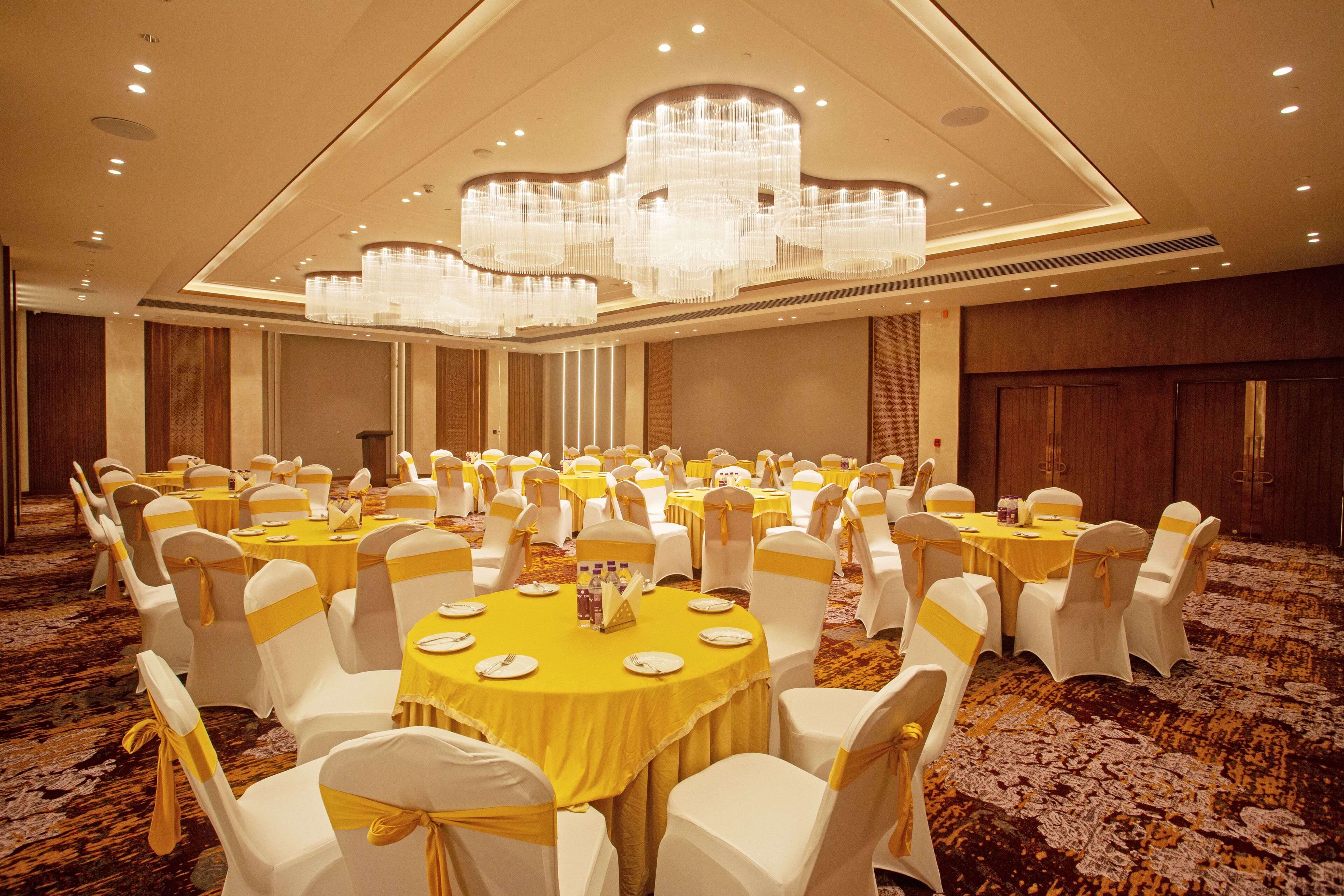 Un salón de banquetes con mesas redondas, sillas blancas y cintas amarillas.