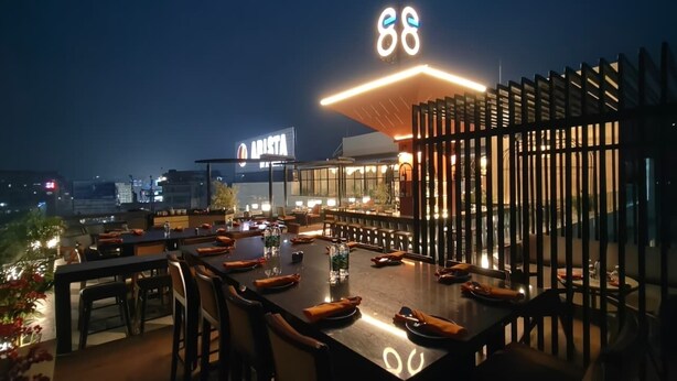 A rooftop restaurant with outdoor seating, a neon sign, and a view of the cityscape at night. - ARISTA BY AMBITION (Guwahati)