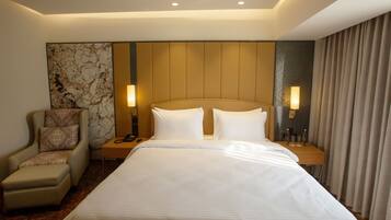 A hotel room with a large bed, a chair, a nightstand, and a lamp.