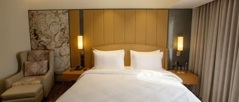 Ein Hotelzimmer mit einem großen Bett, einem Sessel, einem Nachttisch und einer Lampe.