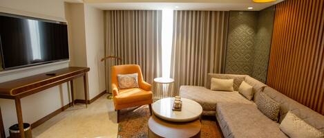 A modern living room with a flat-screen TV, a sofa, an armchair, a coffee table, and a patterned rug.