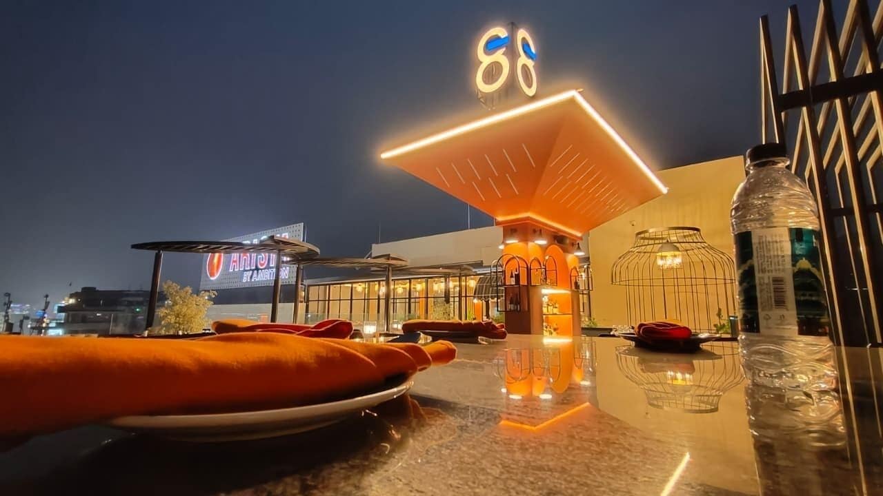 A rooftop dining area with a large illuminated sign, outdoor seating, and a view of the cityscape.