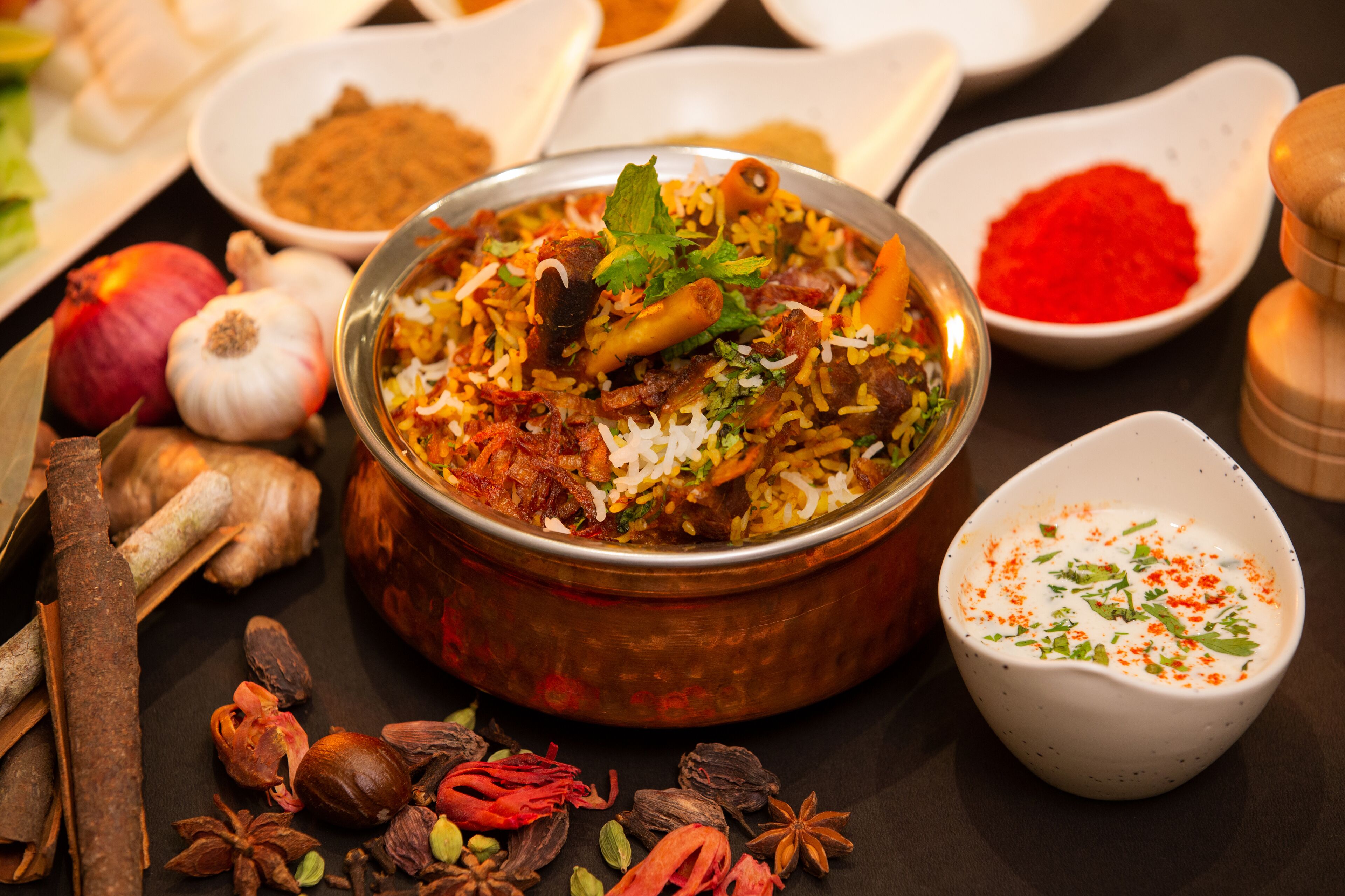 A bowl of biryani with various spices and garnishes around it.