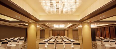 A conference room with rows of white chairs, a large chandelier, and patterned carpet.