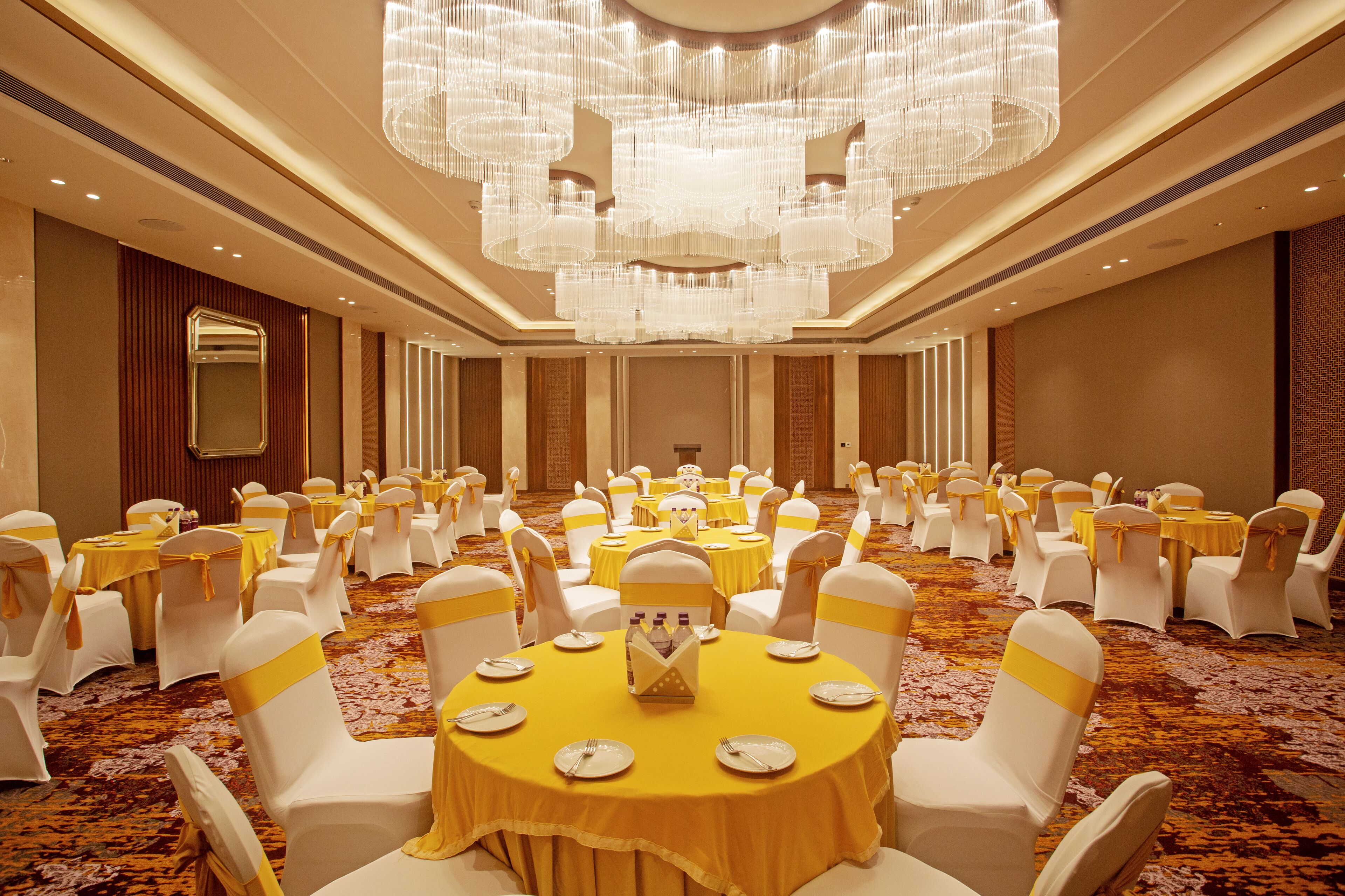 Un salón de banquetes con mesas redondas, sillas blancas y manteles amarillos.
