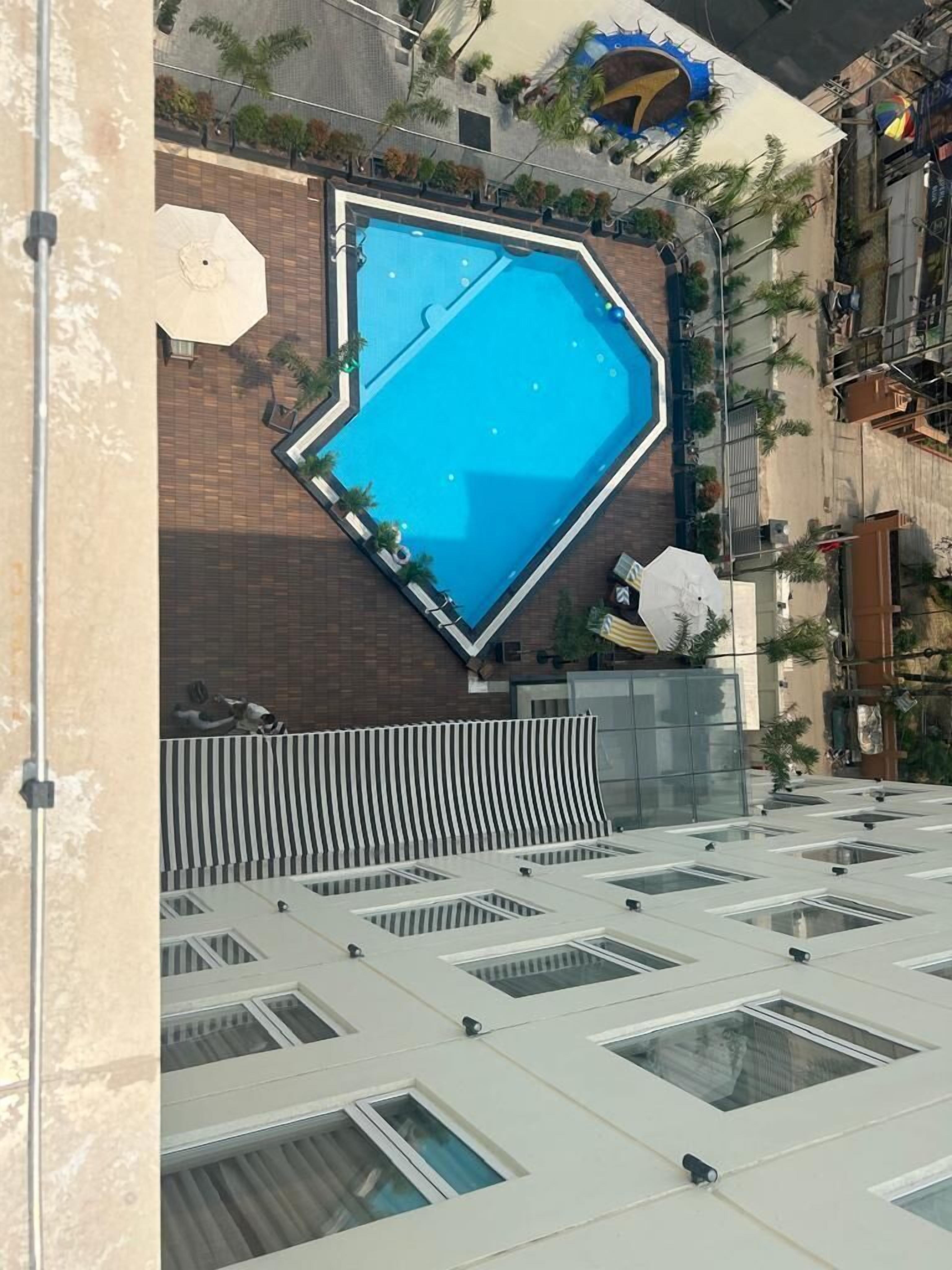 A rooftop pool with a geometric design, surrounded by a brick wall and palm trees.