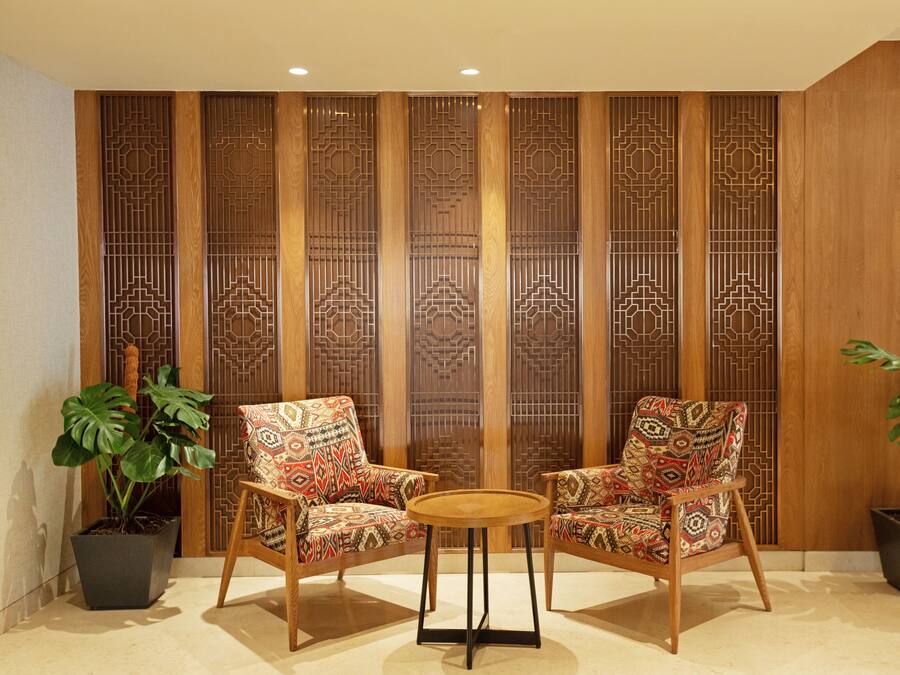 A room with two chairs and a small table, a decorative wooden partition, and potted plants.