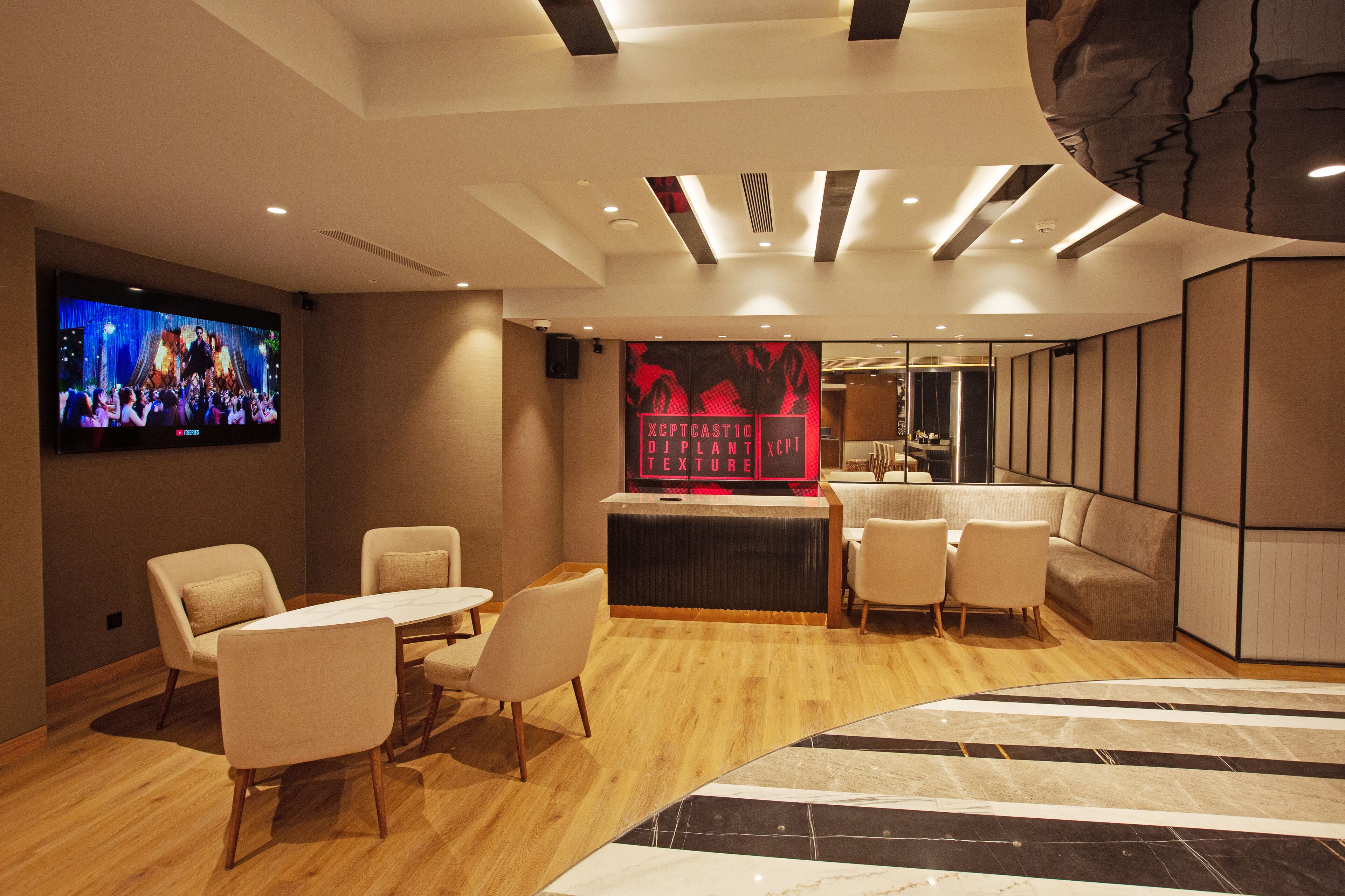 Un vestíbul d'hotel modern amb taulell de recepció, zona de seients i un gran televisor de pantalla plana que mostra un concert.