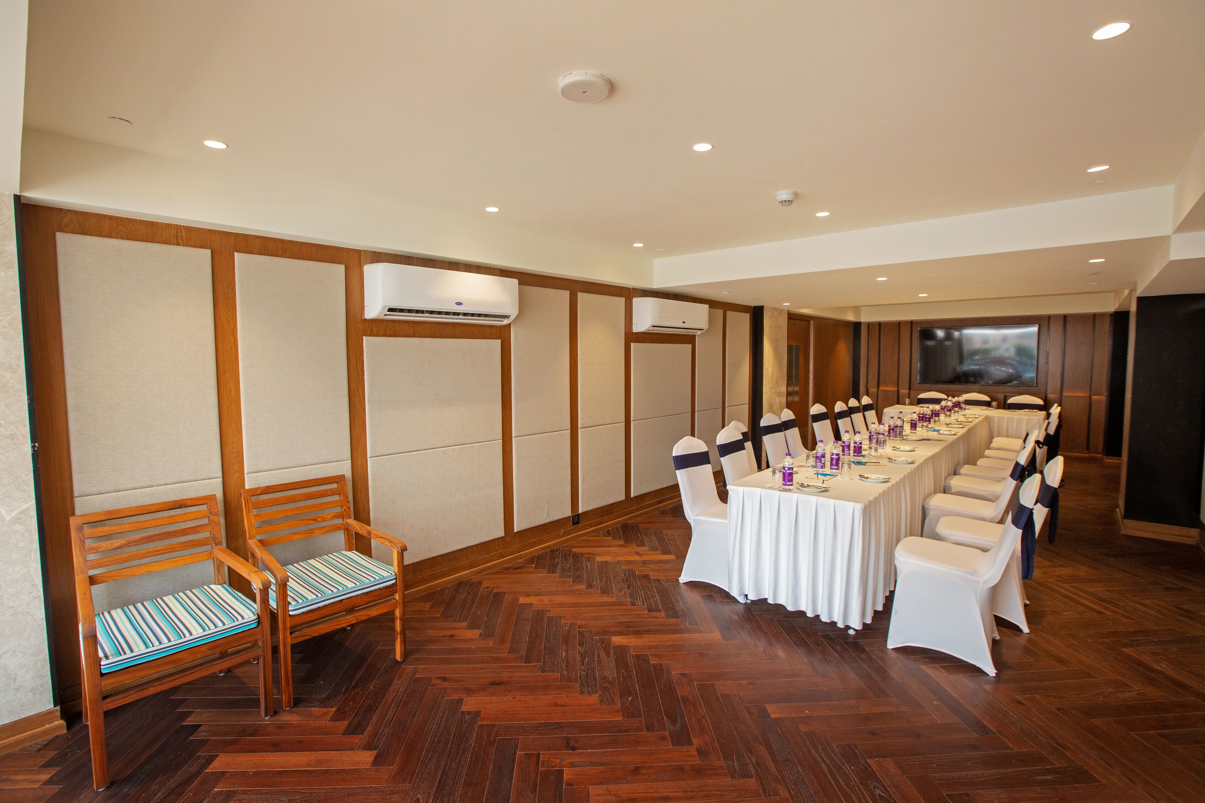 A conference room with a long table, white chairs, and wooden benches.